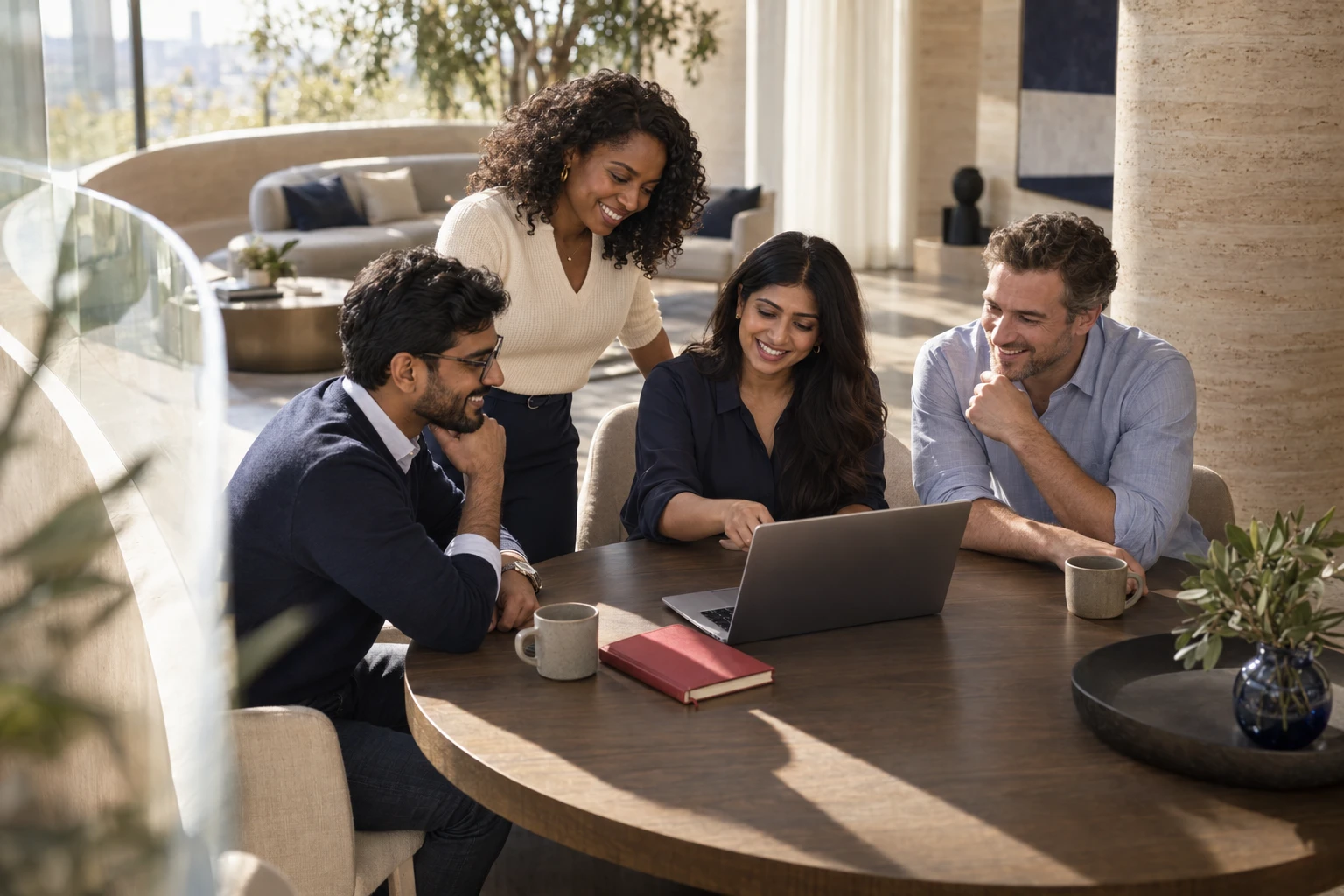 A smiling team collaborating around a laptop in a sunlit studio